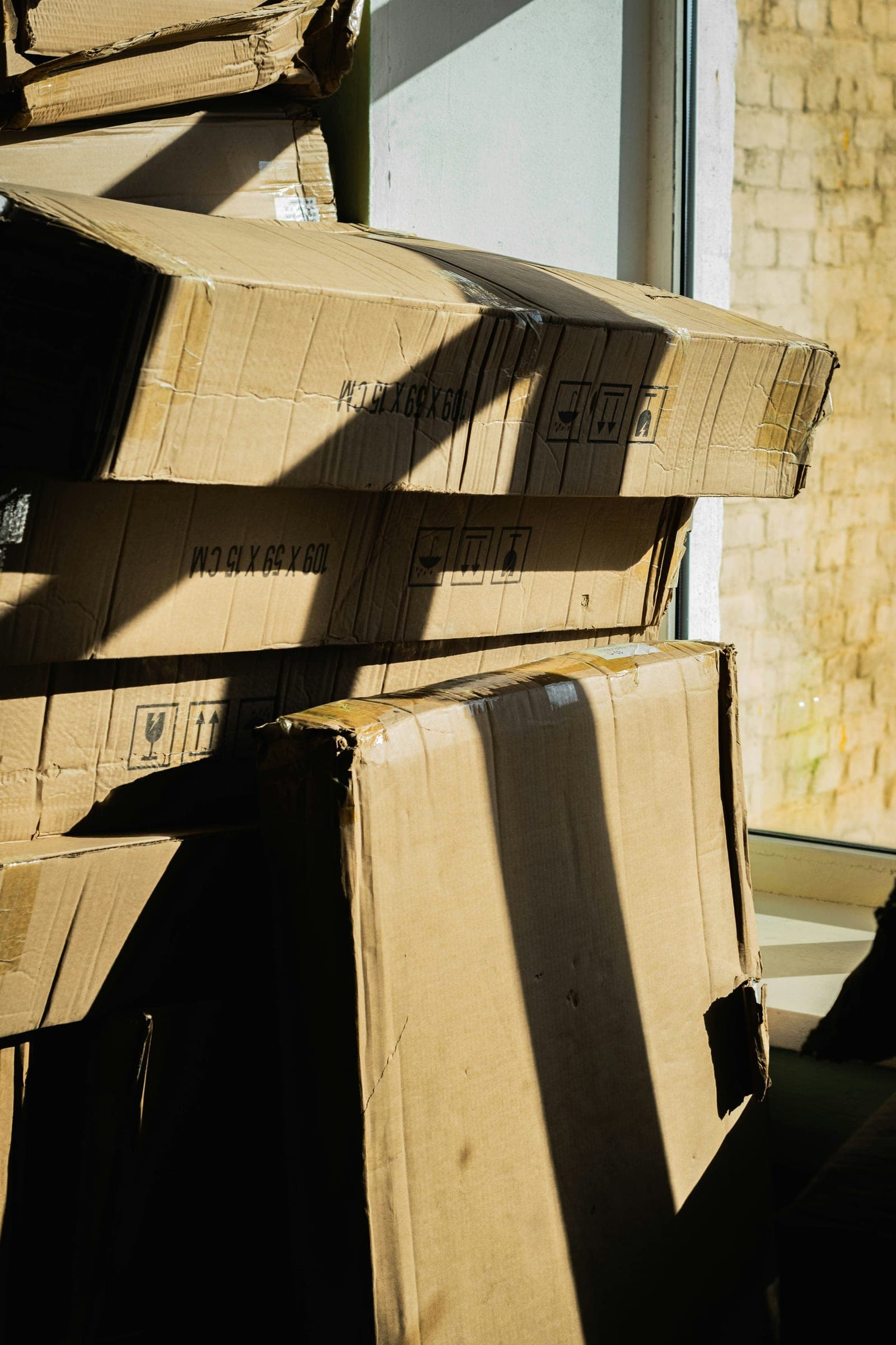A tidy stack of cardboard boxes near a window, lit by strong sunlight.