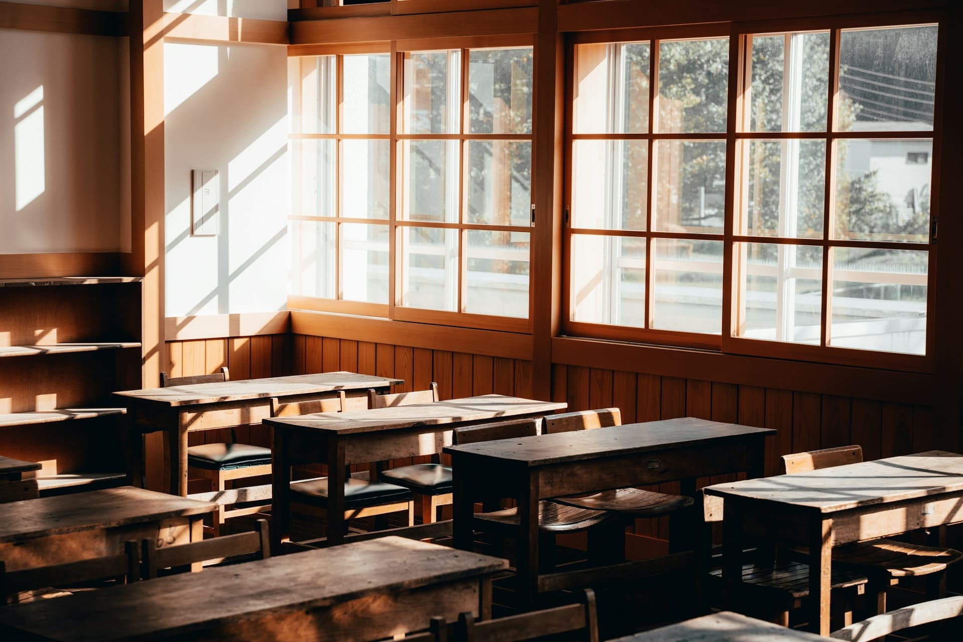 An empty classroom with rows of wooden desks and windows