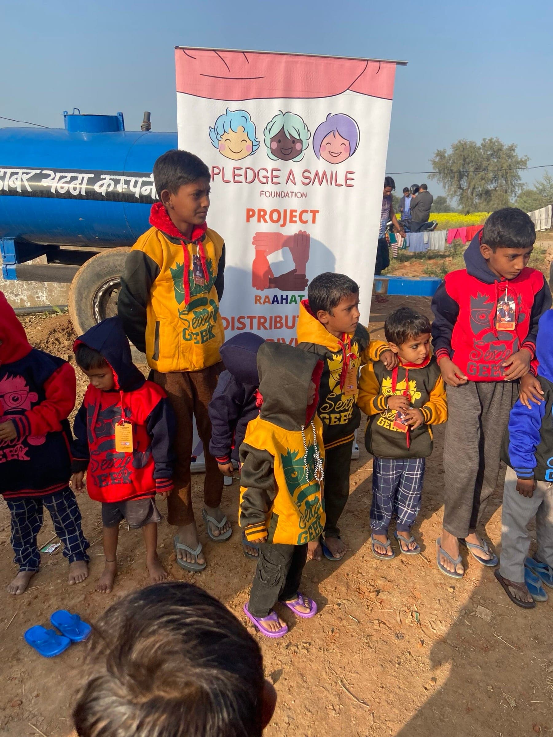 Children in new winter hoodies beside the PAS banner, golden hour at the settlement