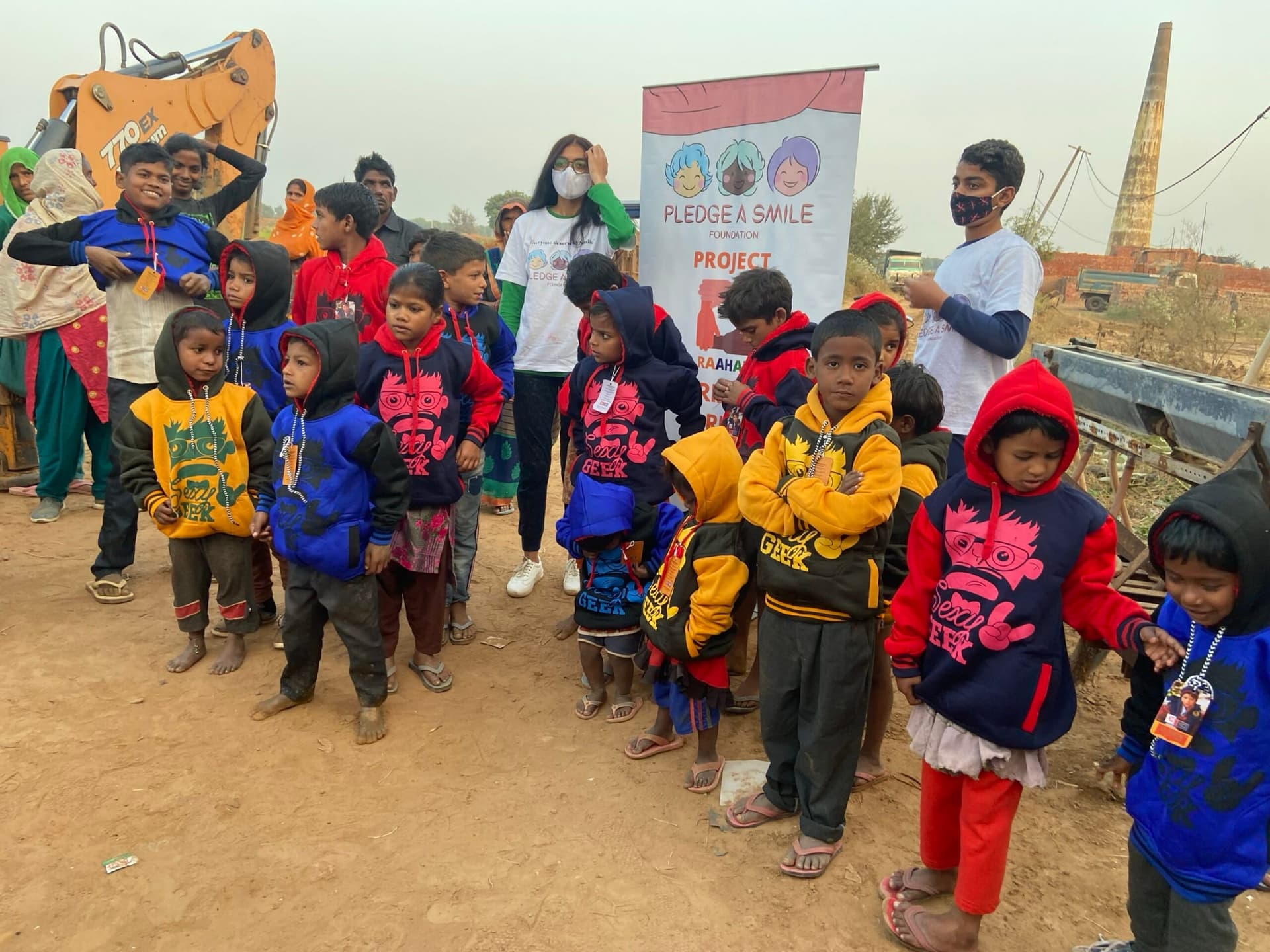 Children in new winter hoodies at a brick-kiln settlement, one boy grinning at the camera