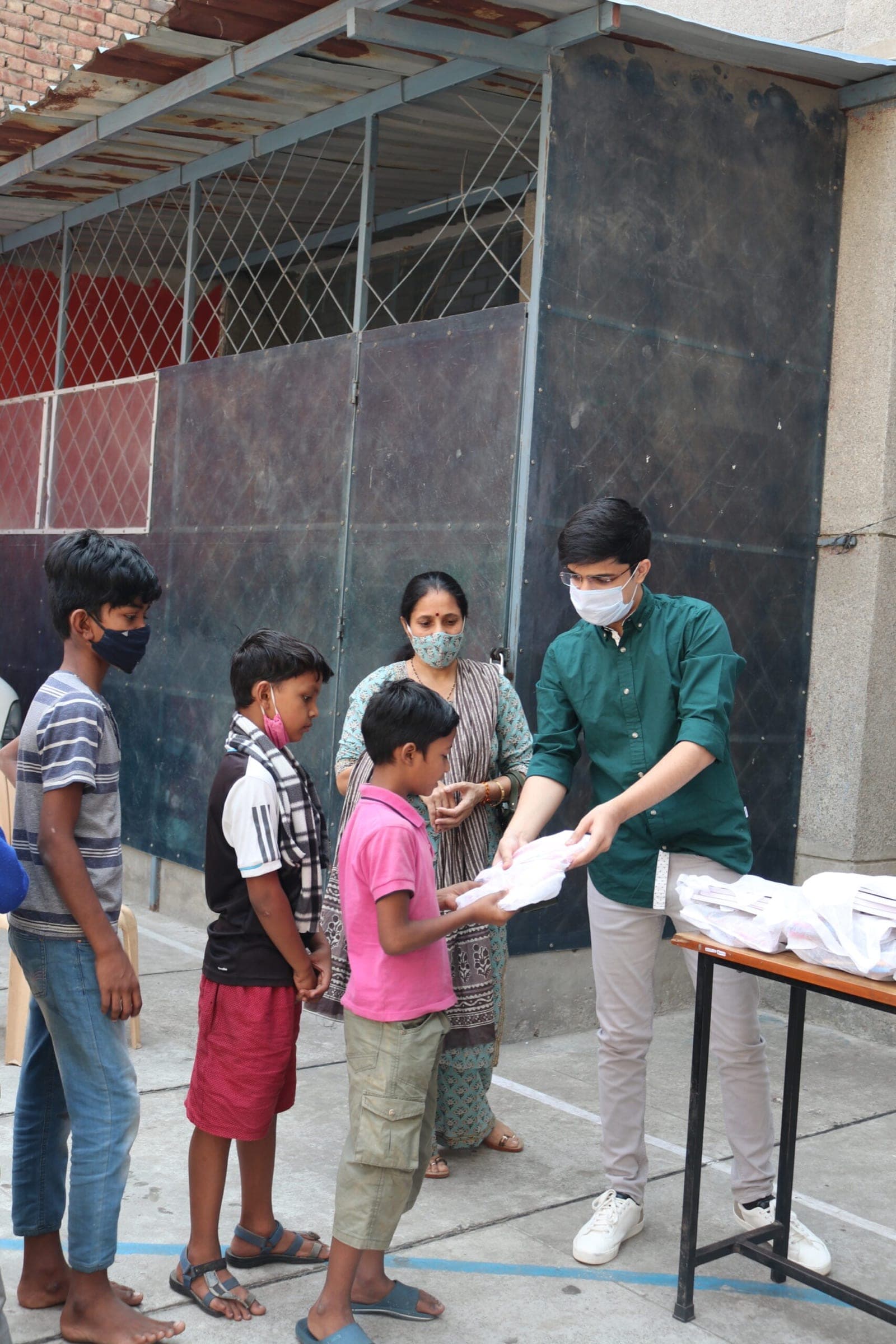 Volunteer handing study/hygiene kits to a queue of boys outside a school gate — candid medium action, sharp, natural light