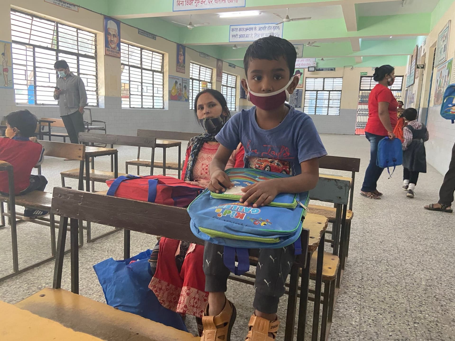 Boy at school desk with new backpack, mother beside him - archival COVID-era documentary (masks visible)