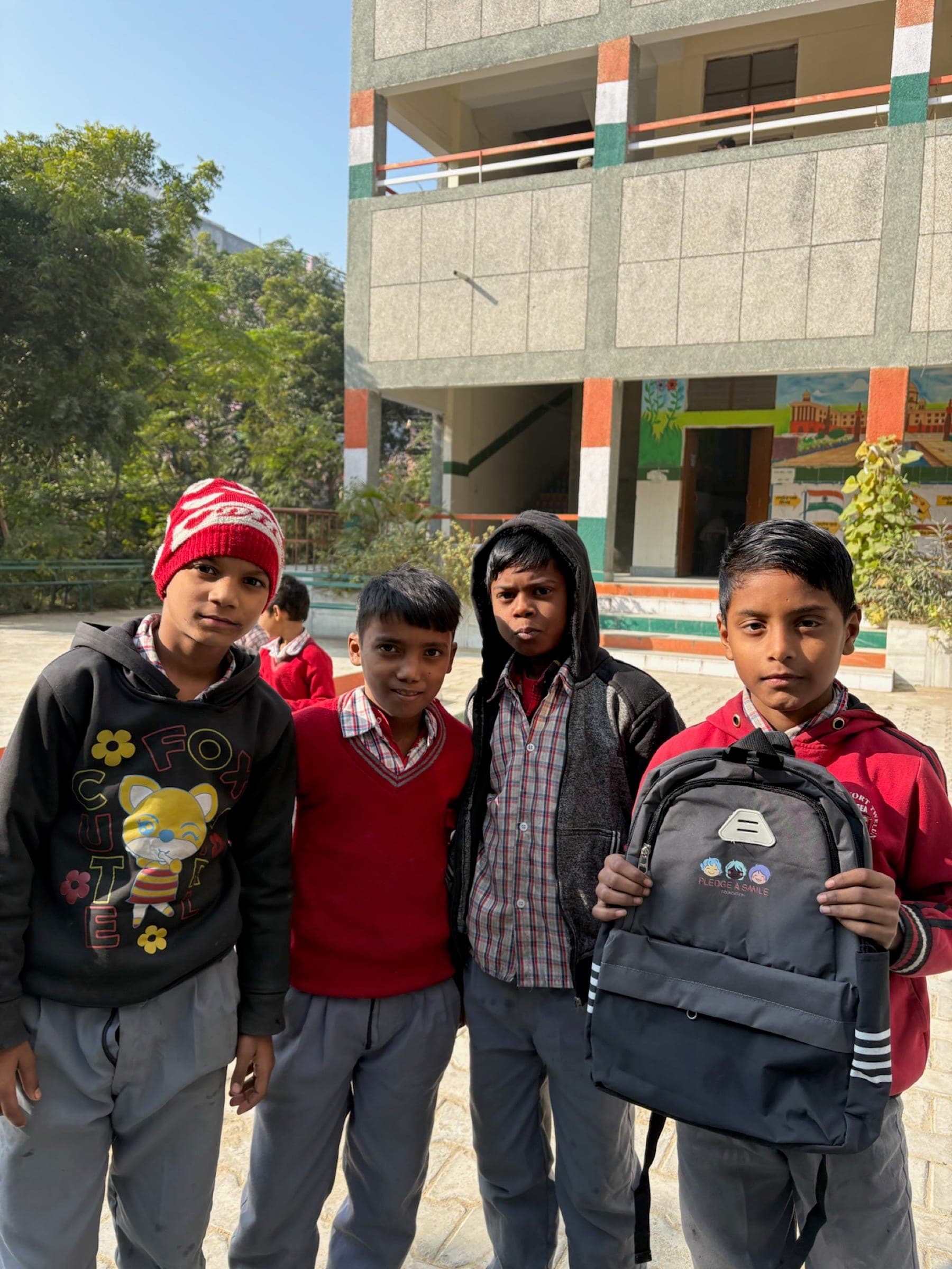 Four boys in winter wear showing a new backpack outside school - medium group