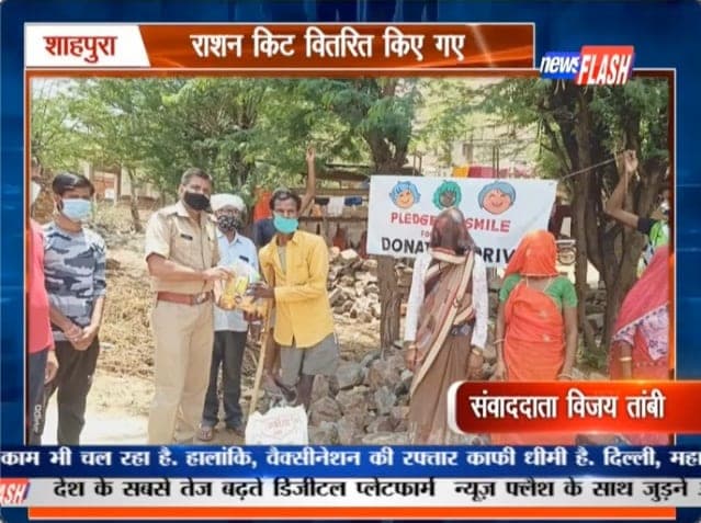 News Flash regional TV still of a Pledge A Smile ration-kit drive in Shahpura, the foundation banner behind a police officer handing over kits