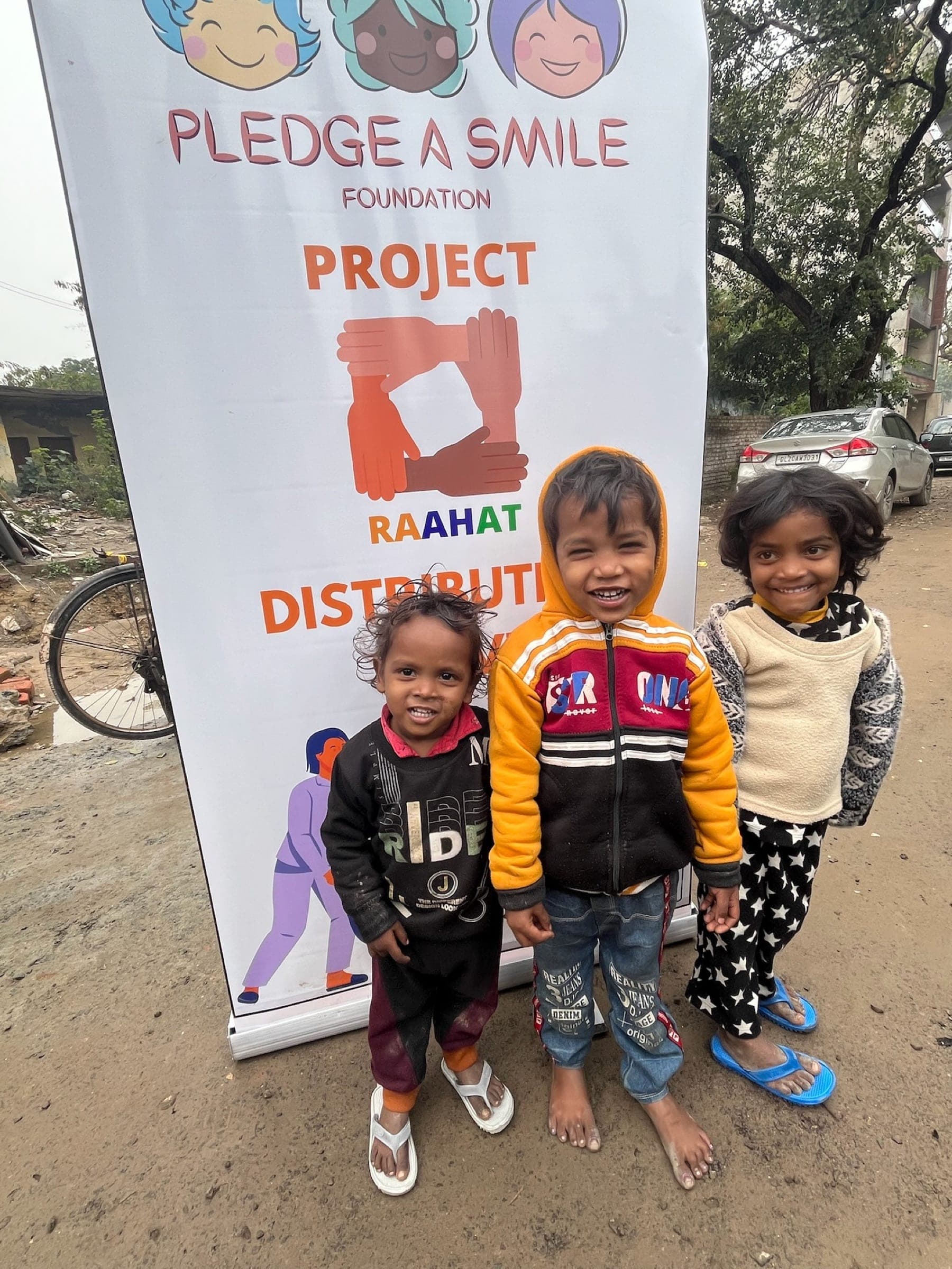 Three small children smiling at the Raahat banner on a winter morning