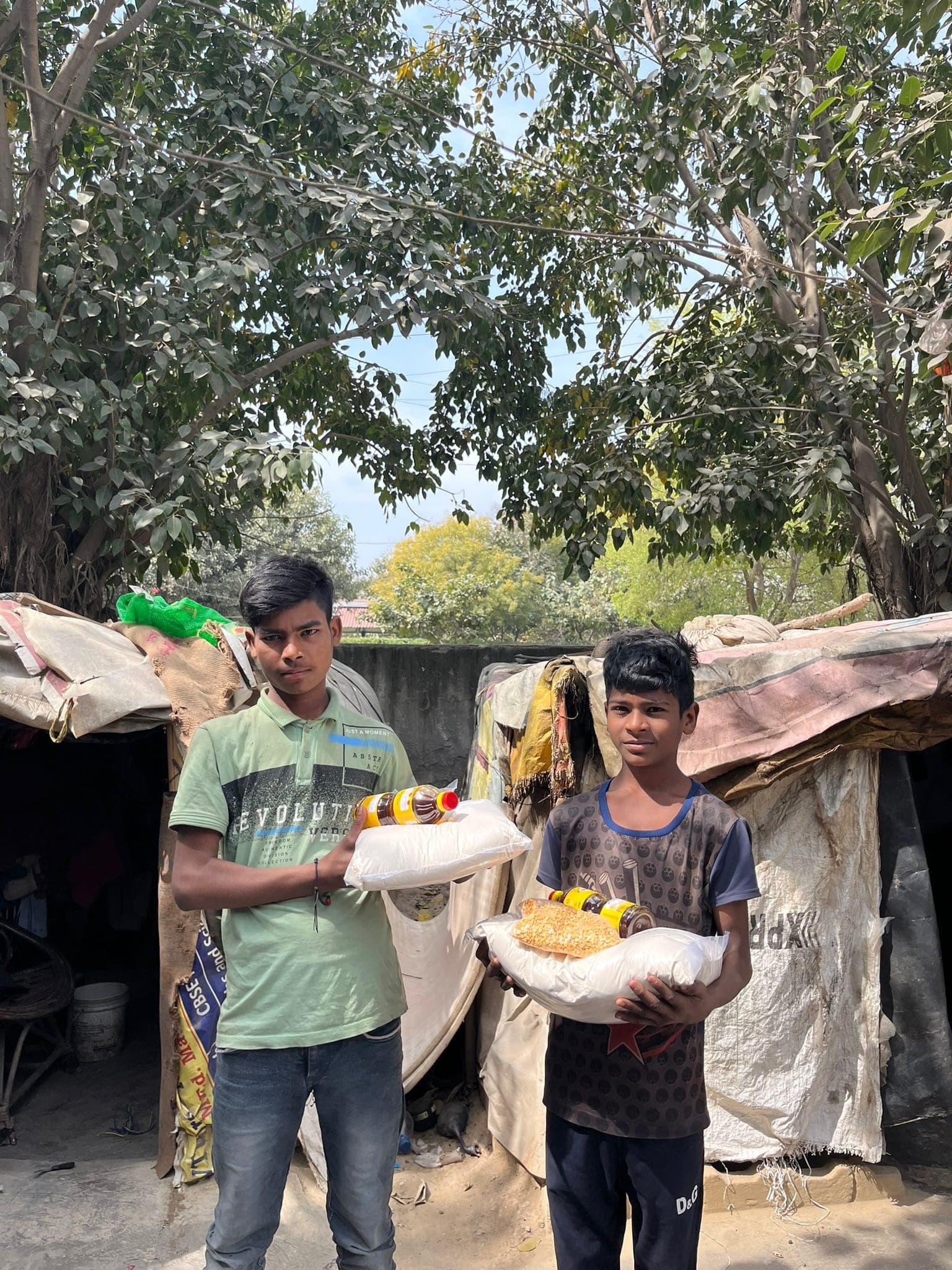 Two boys hold a rice-and-oil ration kit outside their tent home.