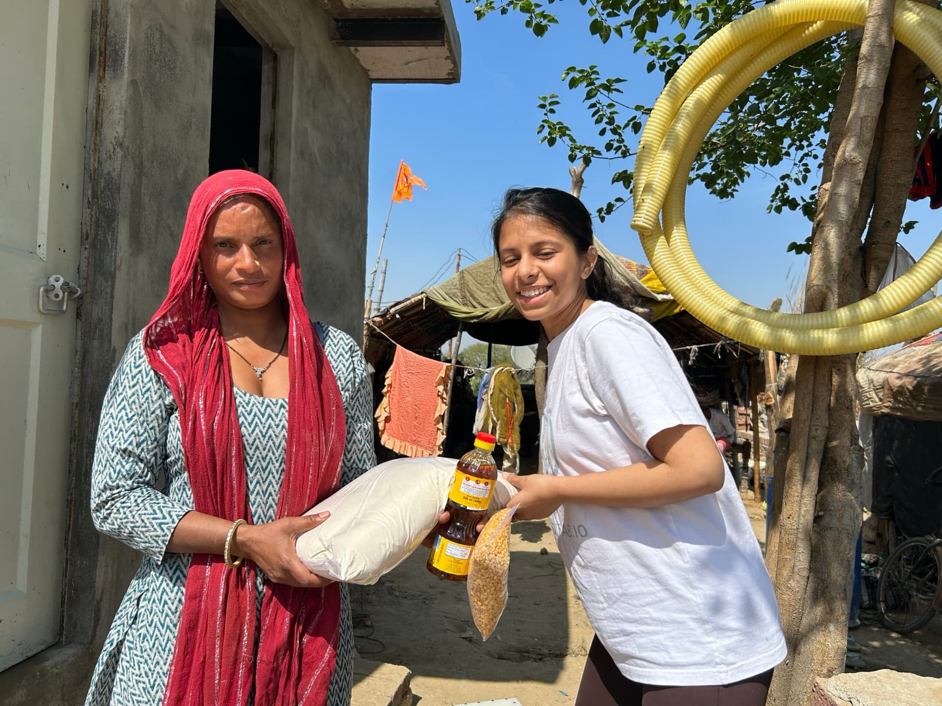 Volunteer and recipient sharing a genuine mutual smile mid-handover of a ration kit — the emotional core of SEVA in one frame; bright natural light, sharp, landscape with breathing room at edges for text overlay.