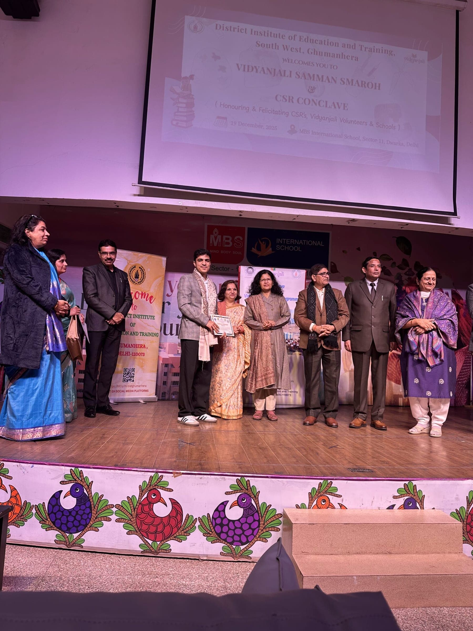 A Pledge A Smile representative receives a certificate on stage at the Vidyanjali Samman Samaroh and CSR Conclave, MBS International School, Sector 11, Dwarka, 19 December 2025.
