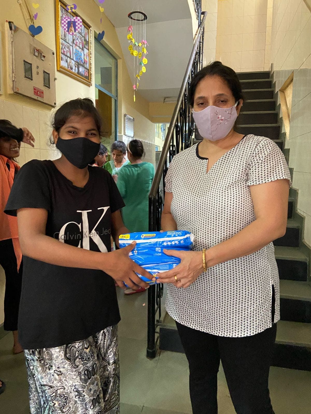 A girl in a black shirt receives a stack of pads from a masked volunteer.