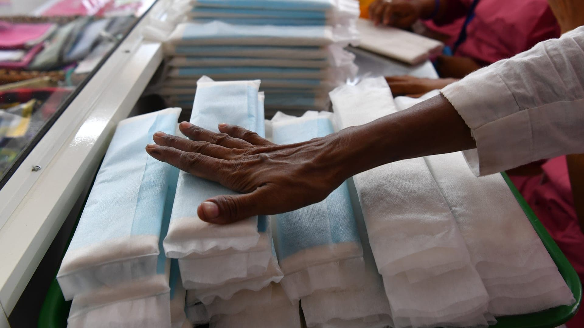 A hand presses down on a stack of sanitary-pad packets — a clean macro of the Noori kit contents.