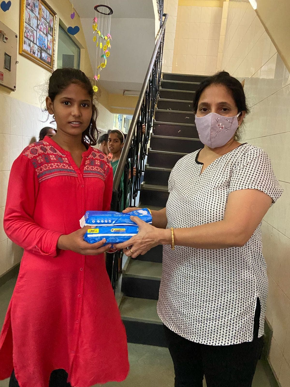 A girl in a red top receives two pad packets in the stairwell.