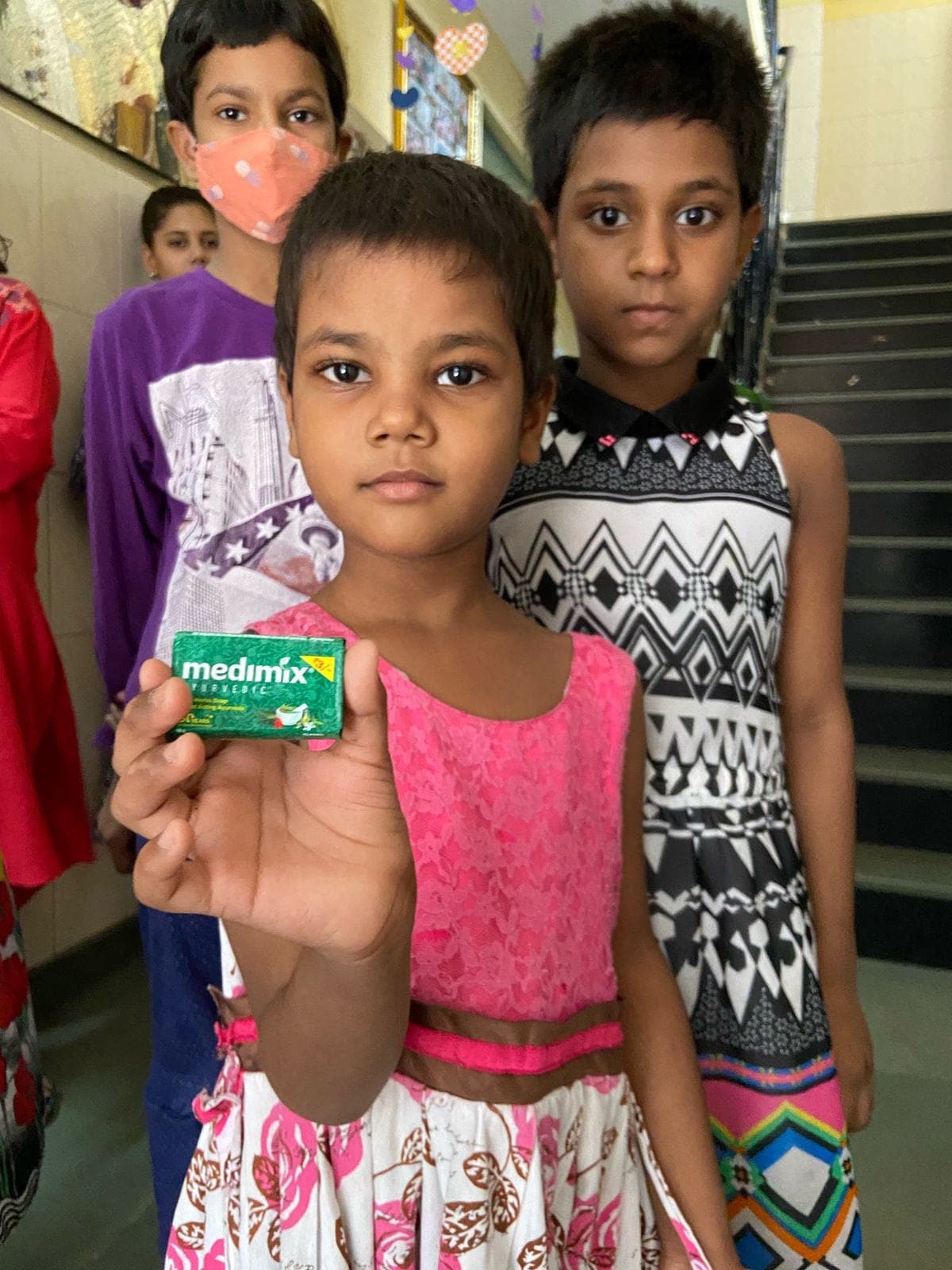 A girl holds a Medimix soap bar from her Noori hygiene kit — the soap-and-hygiene contents beyond pads.