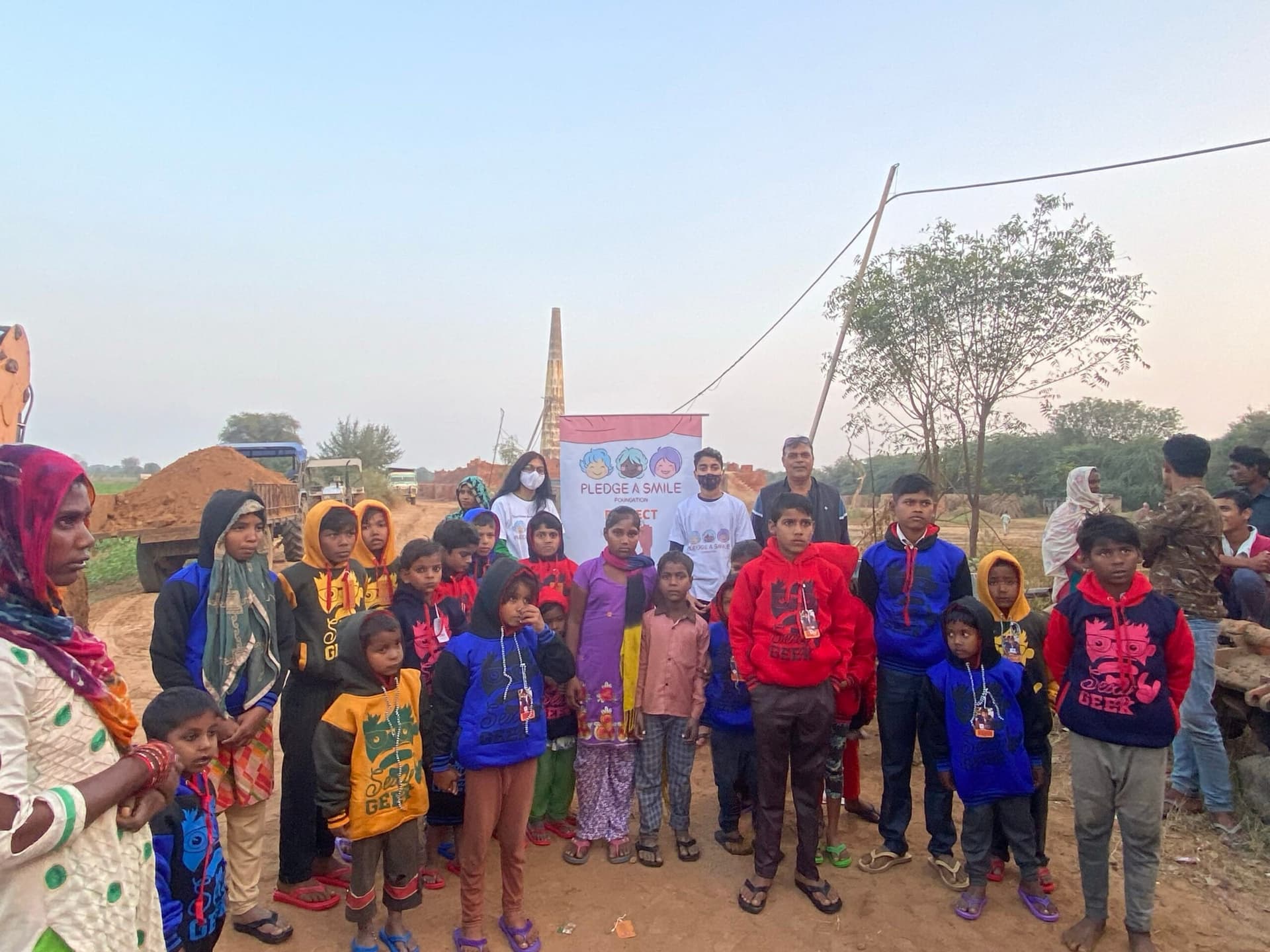 The whole brick-kiln community gathered with volunteers, the kiln chimney and a big open sky behind them.