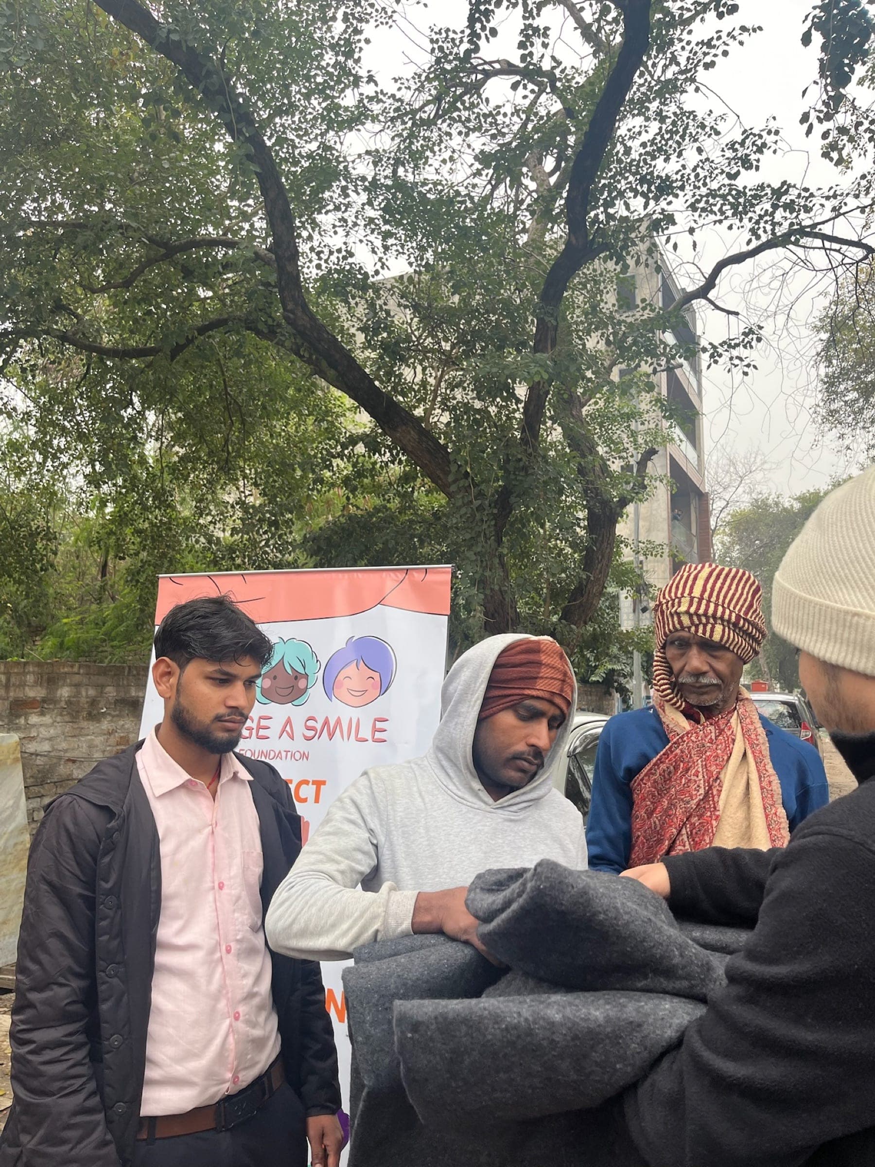 Medium action: blanket handover to men, layered candid with turbaned elder looking on