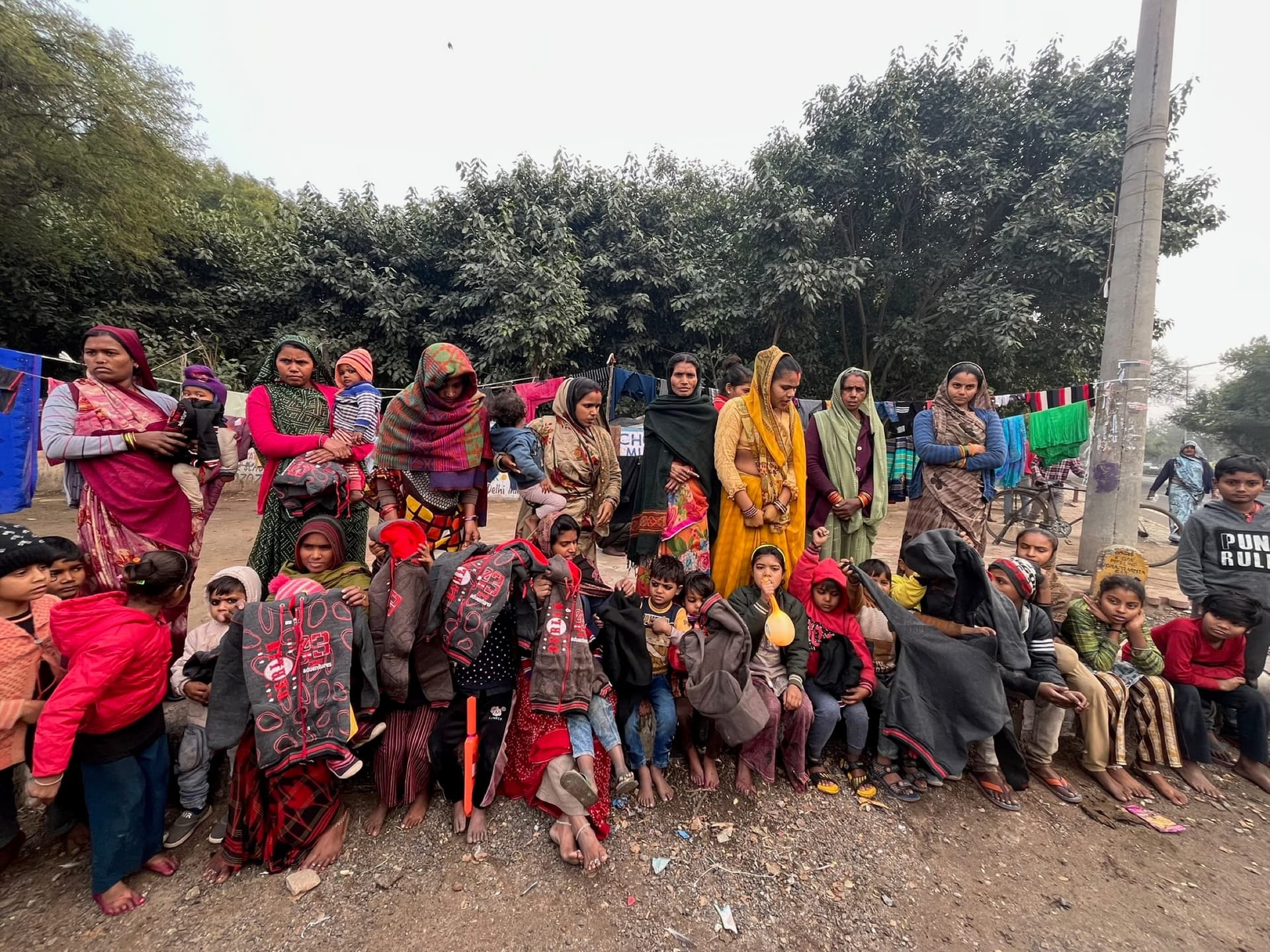 Mothers in bright saris behind rows of children wrapped in new grey blankets