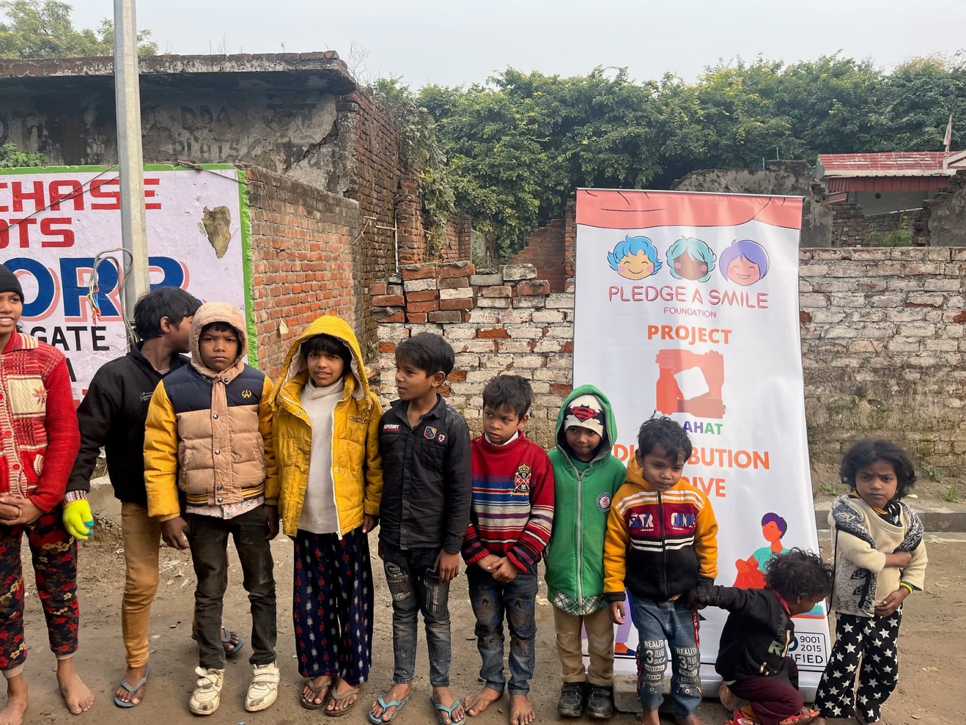 Wide-medium: lineup of children in new winter coats along a brick lane with banner