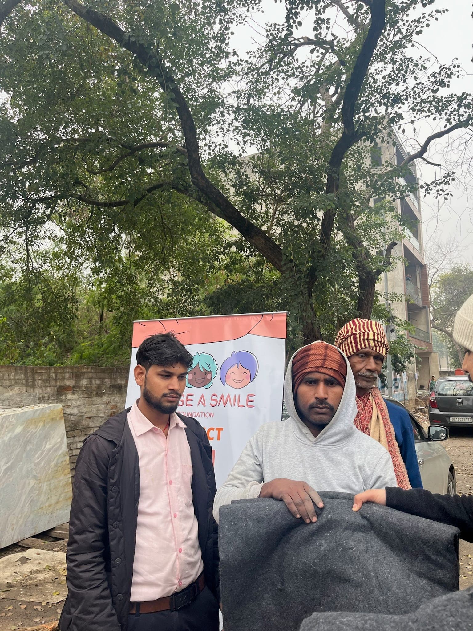 A volunteer in a beanie hands a folded blanket to an older man and woman — a genuine unposed handover.