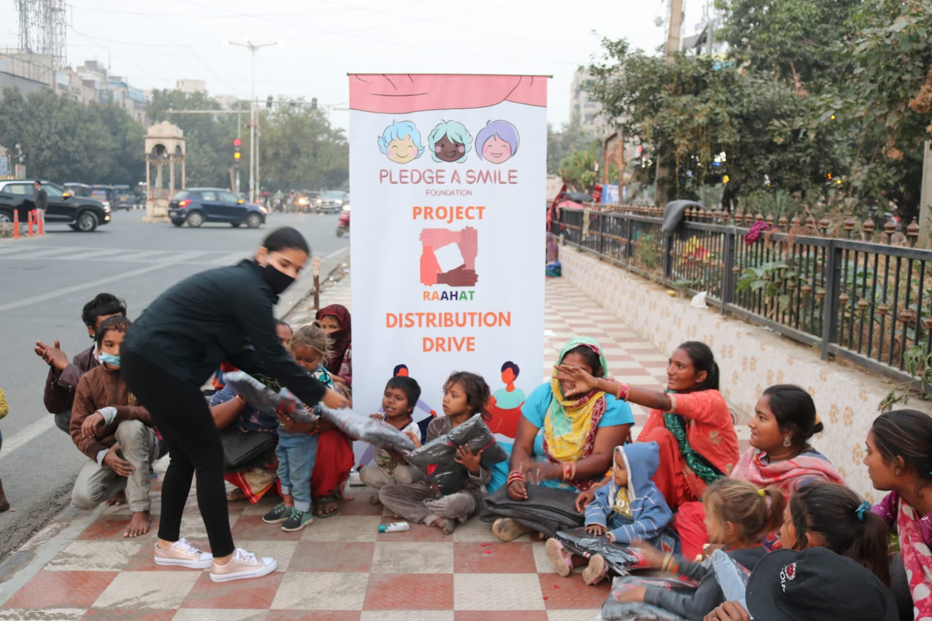 A volunteer hands a folded blanket to a mother and her children seated at a Raahat roadside distribution