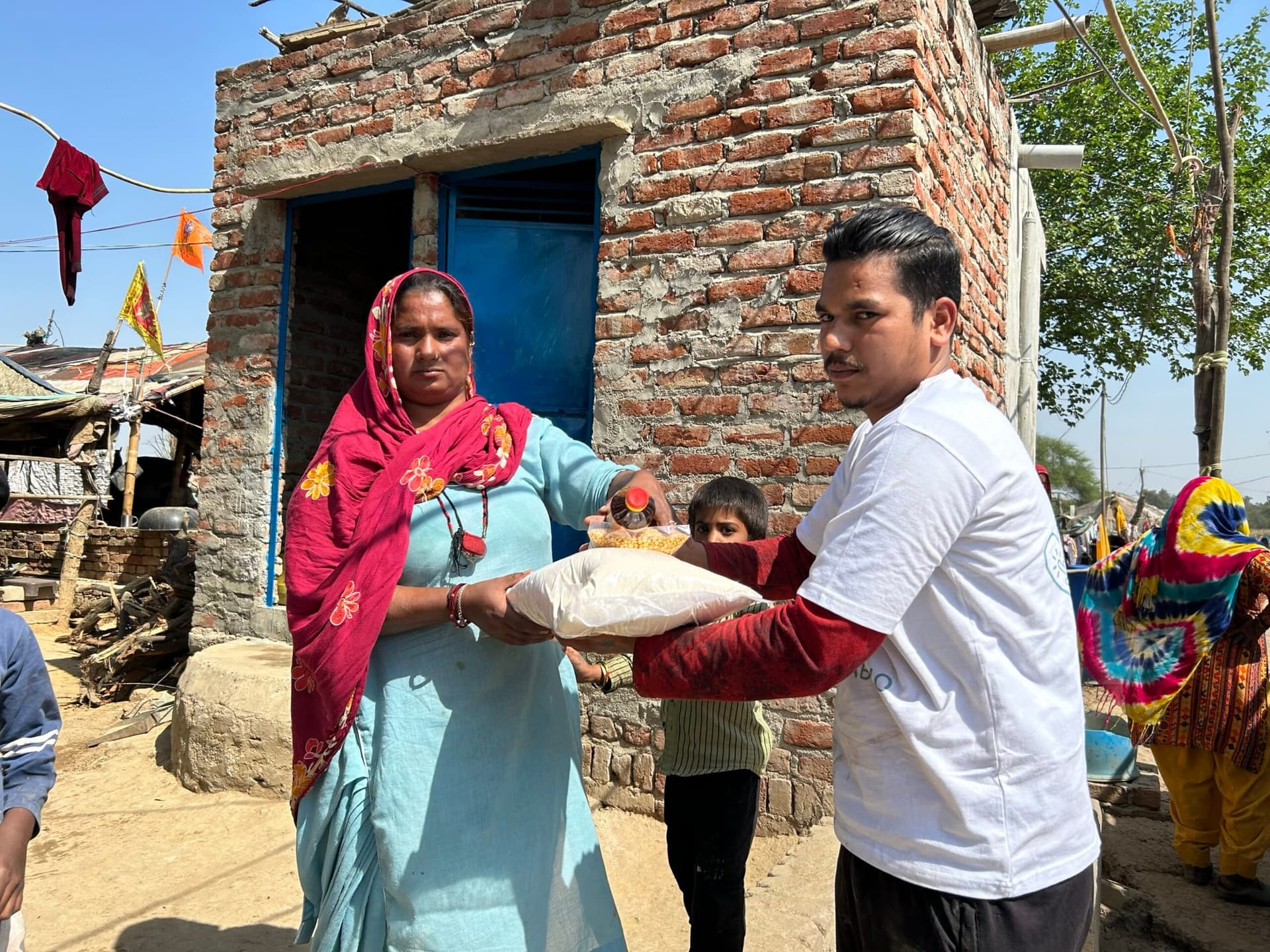 A volunteer hands a ration sack to a woman outside a brick house