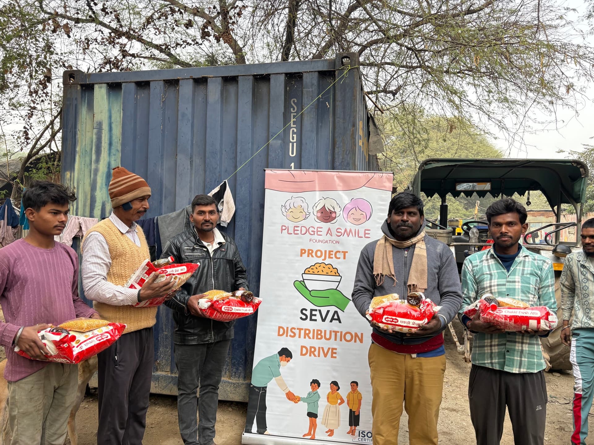 Atta distribution beside a shipping container at a Project Seva drive, SEVA banner visible