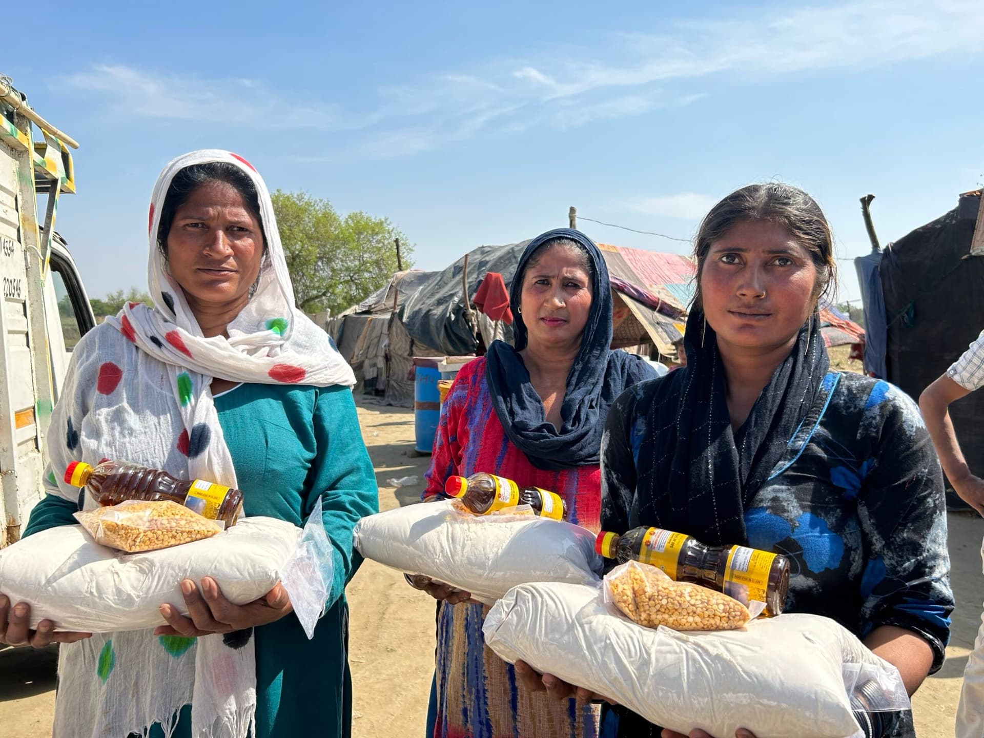Three women holding ration sacks of dal and oil